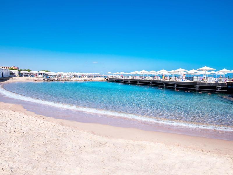 Sandstrand mit klarem blauem Wasser und weißen Sonnenschirmen unter blauem Himmel