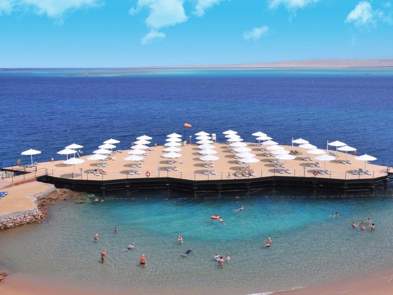Strand mit Sonnenschirmen auf einem Steg über klarem blauem Wasser und Menschen im flachen Wasser