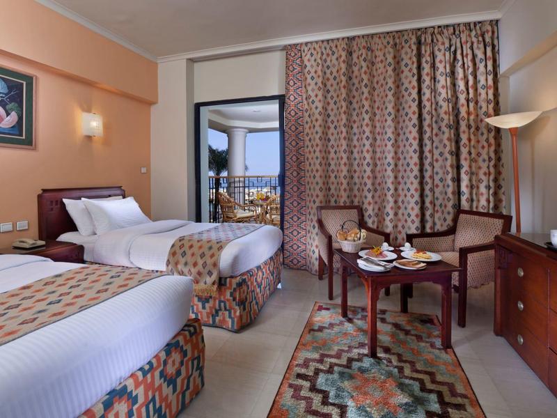 Hotelzimmer mit zwei Einzelbetten, Sitzbereich, Fernseher und Balkon mit Blick auf die Natur.