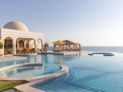 Luxuriöser Pool mit Blick auf das Meer und Pavillons bei klarem Himmel.