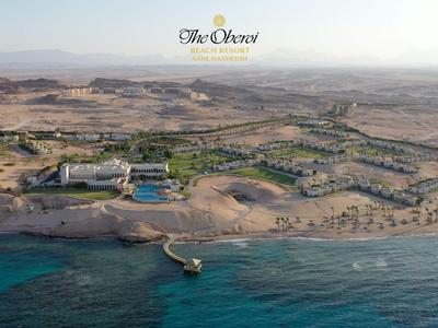 Luftaufnahme eines Resorts an der Küste mit Strand, einigen Gebäuden und klarem Wasser.