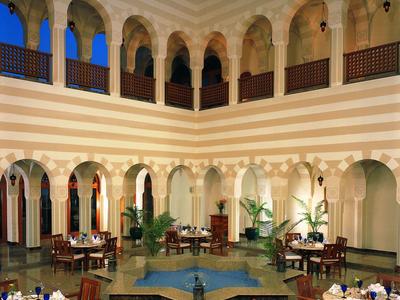 Courtyard with arches, wooden chairs, round tables set for dining, and a central water fountain.