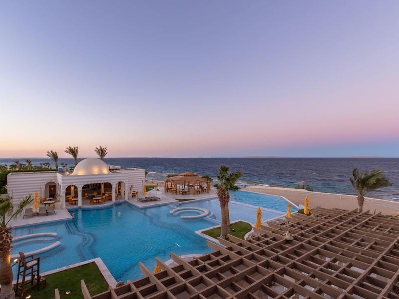 Rooftop pool at sunset with ocean view and palm trees in a luxury hotel.