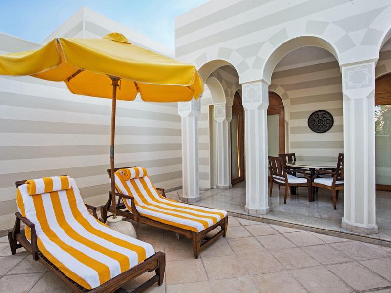 Two yellow-striped lounge chairs under a yellow umbrella on a stone patio with arched doorways.