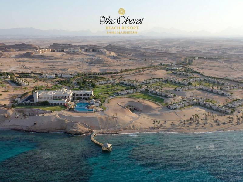 Desert hotel resort with swimming pools, palm trees, and a pier by the blue sea.