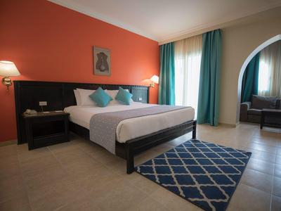 Modernes Schlafzimmer mit großem Bett, blauen Kissen, Teppich und Fenster mit Vorhängen.