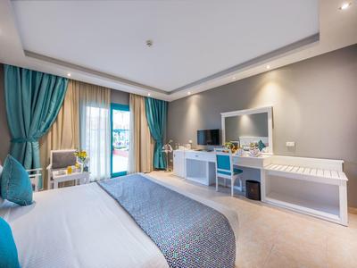 Helles Schlafzimmer mit blau-grauen Vorhängen, Bett, Schreibtisch und Balkon mit Tageslicht.