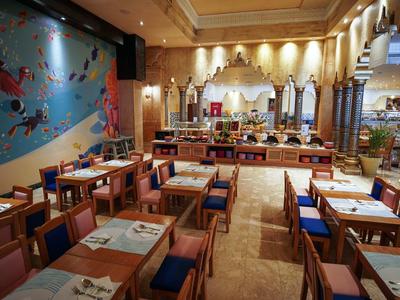 Modernes Restaurant mit blauer Wand, vielen Holztischen und blauen Stühlen, hellem Boden und Säulen.
