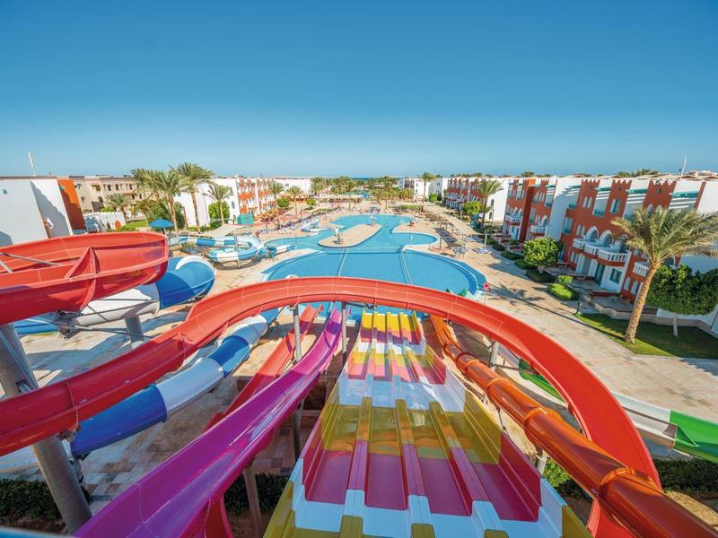 Bunte Wasserrutschen auf einem großen Poolresort mit weiß-roten Gebäuden und klarem Himmel.