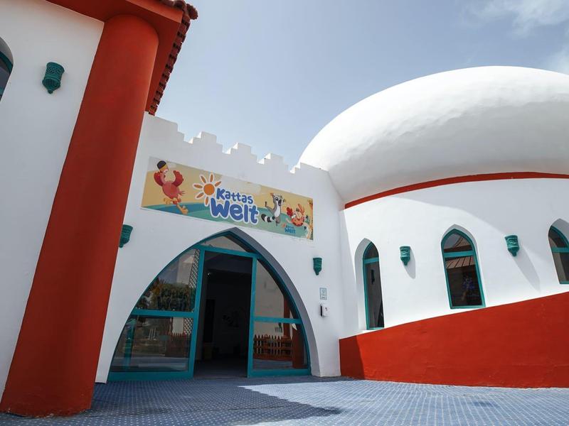 Ein modernes Gebäude mit weißen, runden Wänden und roten Säulen unter blauem Himmel.