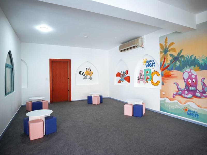 Flur mit weißen Wänden, bunten Sitzwürfeln und kindlichen Wandbildern, darunter Strandmotiv.