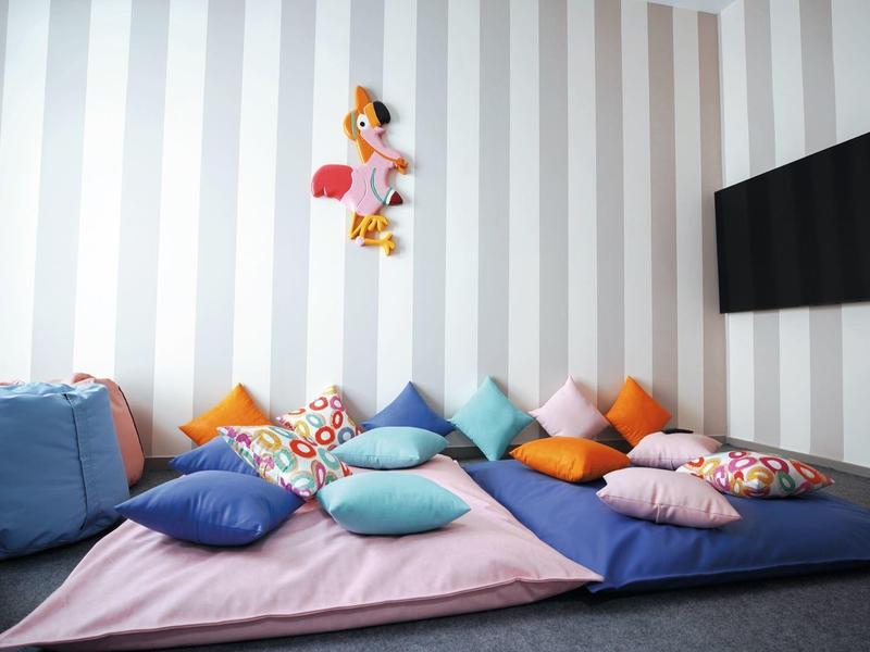 Gemütliche Sitzecke mit bunten Kissen, weichen Decken und flachem Fernseher an gestreifter Wand.