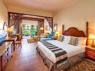 Gemütliches Hotelzimmer mit Doppelbett, Holzmöbeln, Fernseher und Blick auf Terrasse und Garten.