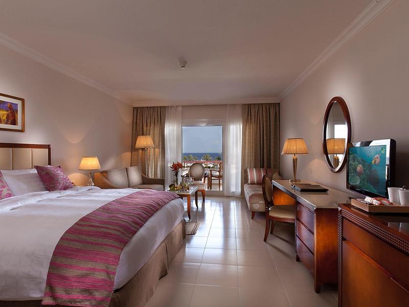 Habitación de hotel elegante con cama grande, muebles de madera y vista desde el balcón.