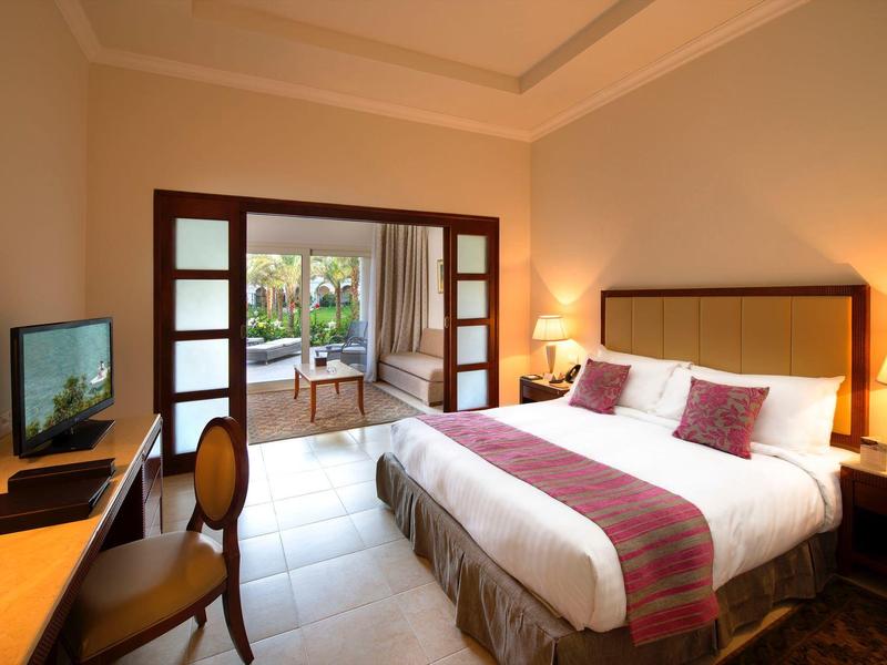 Habitación de hotel luminosa con cama grande, escritorio, televisor y acceso a terraza con vista al jardín.