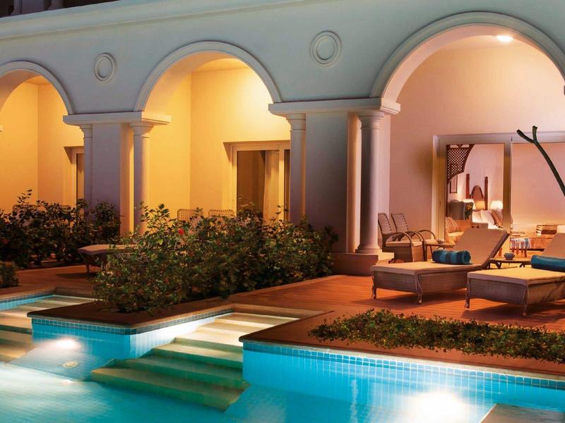 Piscina iluminada y área de descanso con sofás en un hotel por la noche.