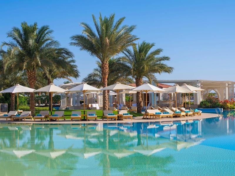 Gran piscina con tumbonas y palmeras en un lujoso resort hotelero.