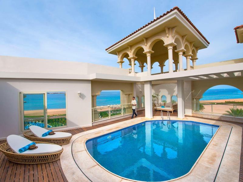 Piscina azul clara en terraza con vista al mar y muebles para relajarse, clima soleado.