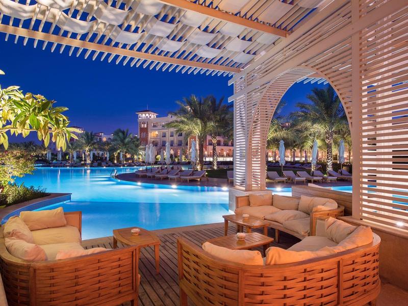 Lounge acogedora con muebles de mimbre junto a piscina iluminada en hotel tropical por la noche.