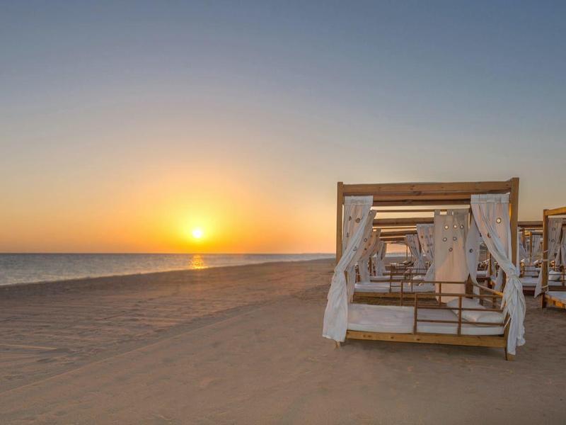 Puesta de sol en la playa con camas cubiertas blancas sobre la arena.