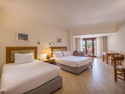 Helles Hotelzimmer mit zwei Betten und Zugang zu einem Balkon mit Gartenblick.