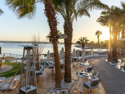 Zonnig hotelzwembadgebied met palmbomen en uitzicht op zee bij zonsondergang.