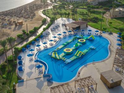 Pool area with water attractions and sun loungers beside a sandy beach and green areas.