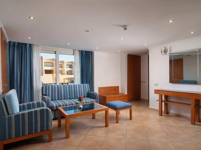 Bright hotel lounge with blue armchairs, sofa, wooden table, and large wall mirror.