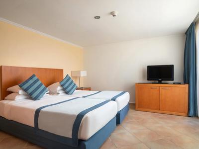 Bright hotel room with double bed, TV, and large window with curtains.