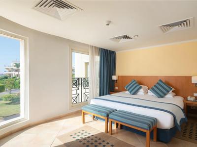 Bright hotel room with large bed, blue pillows, and garden view.