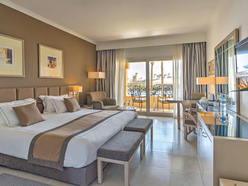 Bright hotel room with two beds, balcony, and modern furnishings.