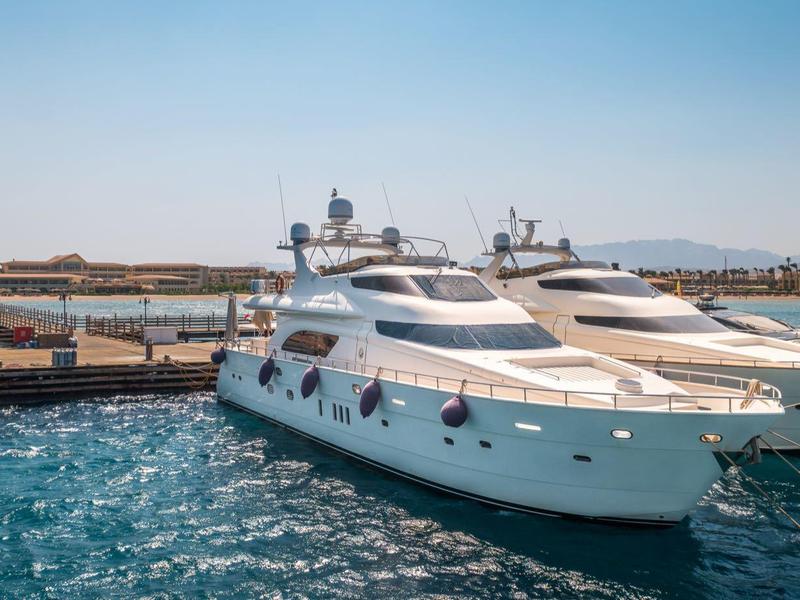 White luxury yacht docked at pier on calm blue water under sunny sky.
