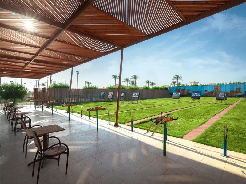 Outdoor terrace with chairs overlooking a lawn with paths and blue buildings under a blue sky.
