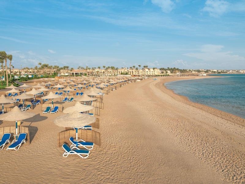 Long sandy beach with sun loungers and umbrellas by still sea.