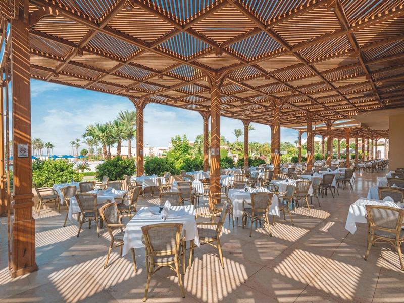 Covered outdoor seating area with tables and chairs in a sunny hotel garden.