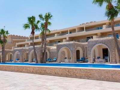 Hotel with stone arches, pool, and palm trees under a clear blue sky.