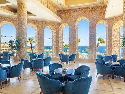 Innenraum eines Hotels mit blauen Sesseln und Meerblick durch große Bogenfenster.