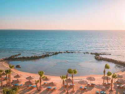 Beach resort with sandy shore, palm trees, and calm sea at sunset.