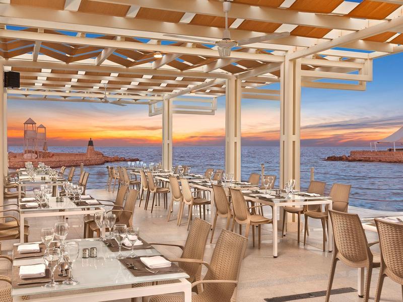 Open-air restaurant with white tables, chairs, and sea views at sunset.