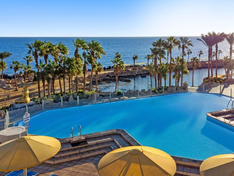 Large pool with palm trees and ocean view at sunset in a tropical resort.