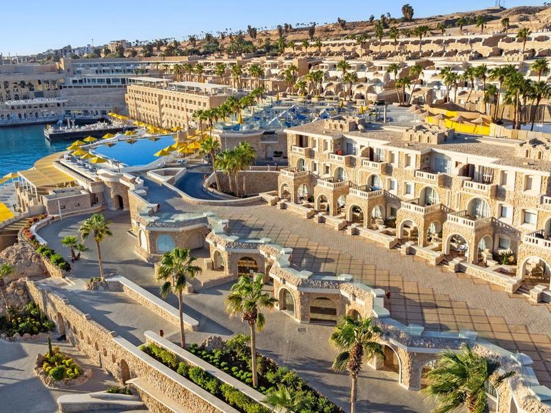 Luxury resort with pools by the coast, surrounded by palm trees and sea views.