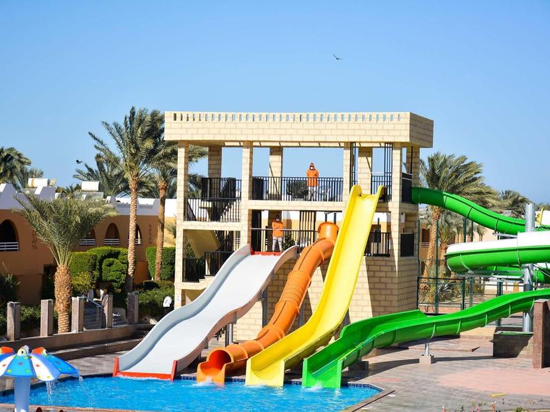 Colorful water slides leading into a pool at a sunny vacation resort with palm trees.