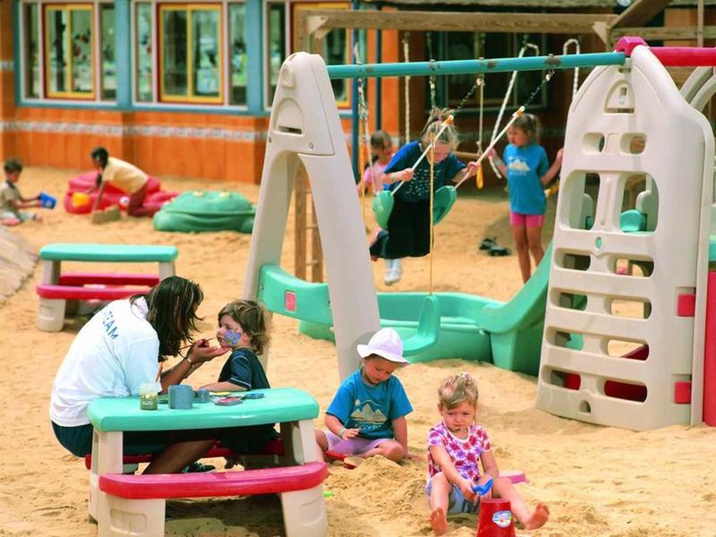 Children playing on sandy playground with colorful swings and climbing equipment.