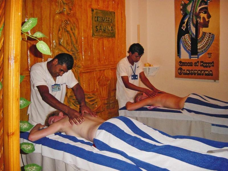 Two men receiving back massages in a spa room with wooden décor and a Pharaoh poster.