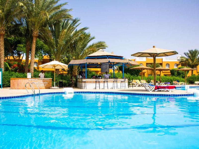 Outdoor pool with sun loungers and shaded umbrellas at a tropical resort.