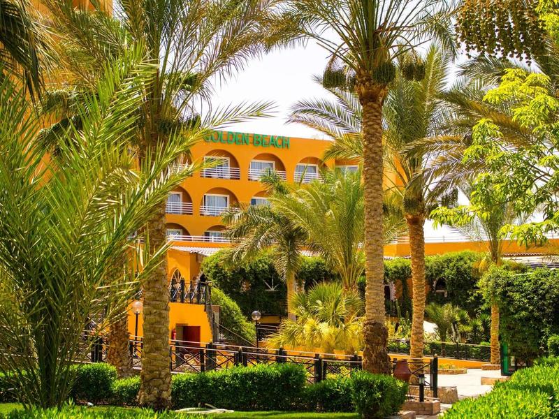 Yellow hotel building surrounded by tall palm trees and lush green garden.