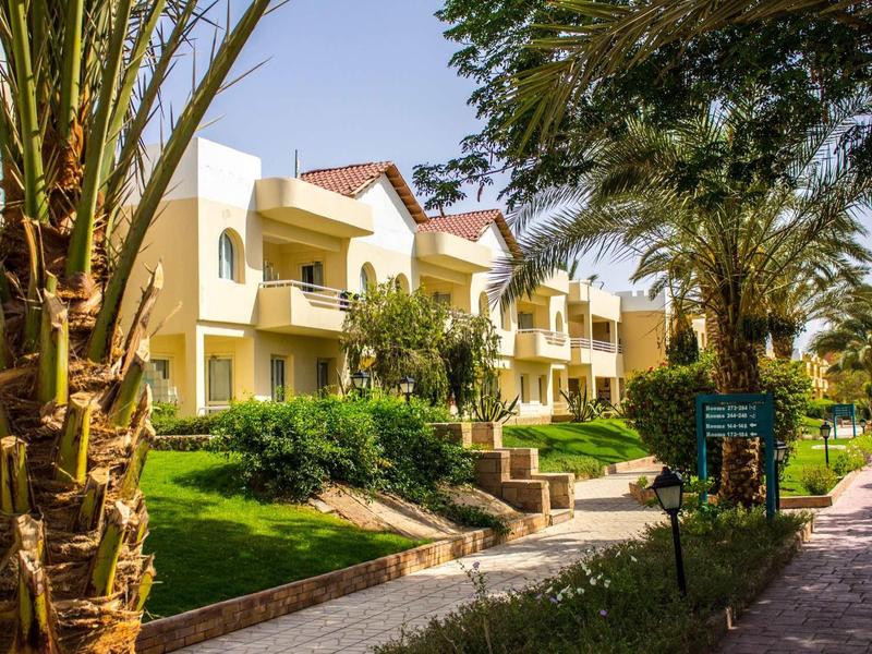 Yellow two-story hotel buildings surrounded by lush green plants and palm trees along a stone pathway.