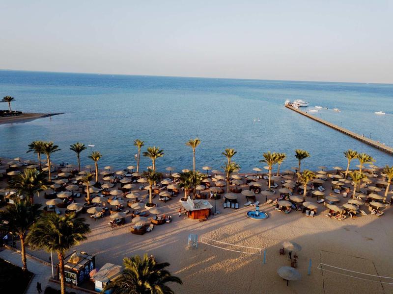 Beach resort with palm trees, sun umbrellas, and a calm sea under a clear sky.