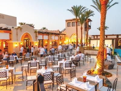 Outdoor-Restaurantbereich mit zahlreichen Tischen, Stühlen, Palmen und entspannter Abendbeleuchtung.
