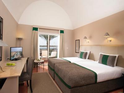 Helles Hotelzimmer mit zwei Betten, Schreibtisch, Fernseher und Balkontür mit Ausblick.